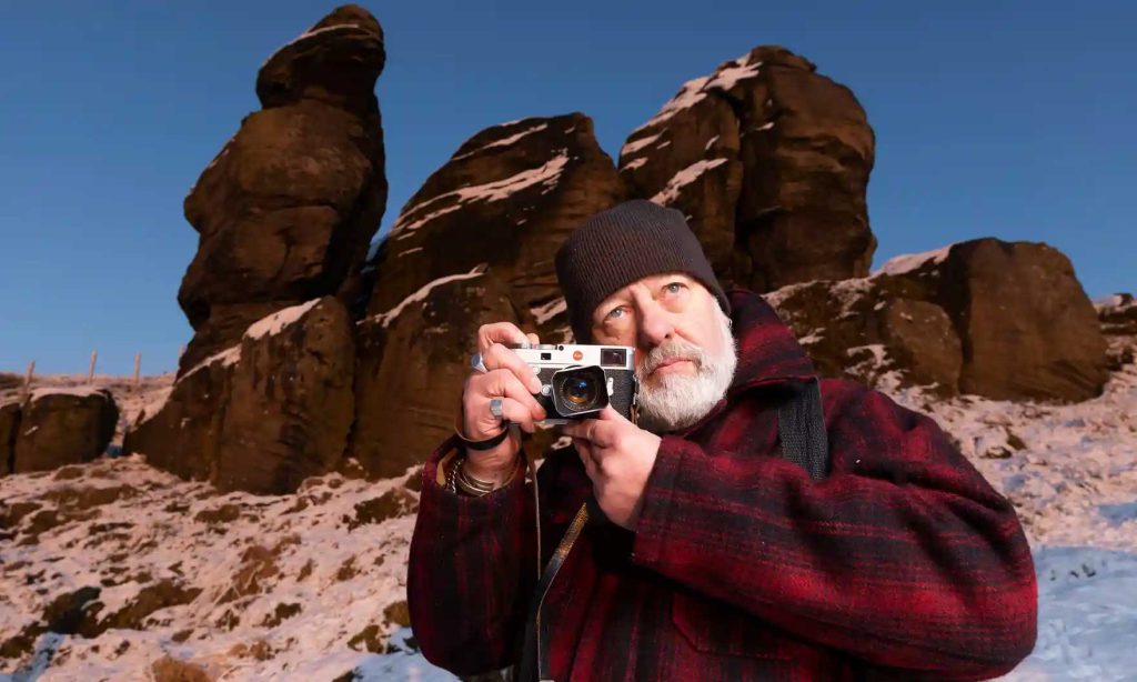 A man holding an old school camera with an unusual rock formation in the background